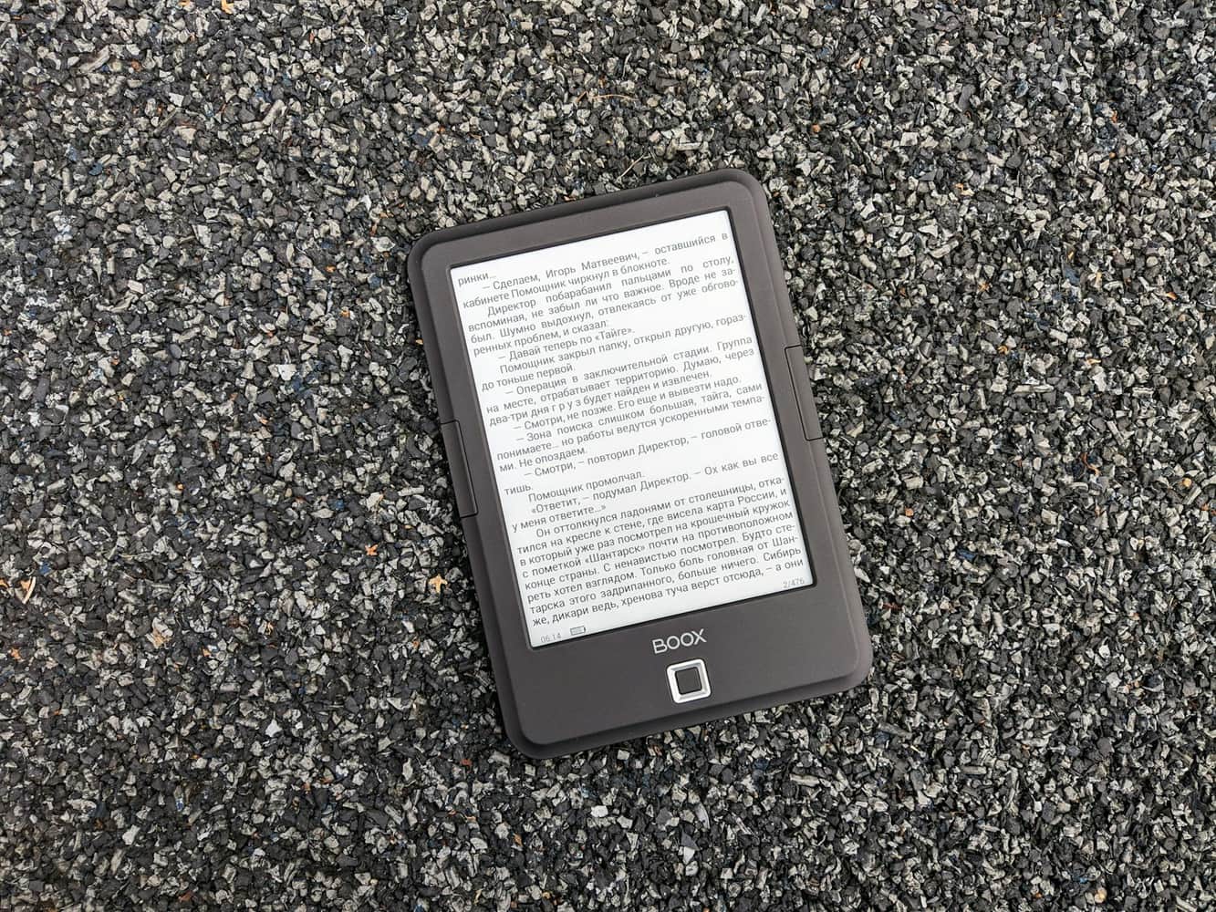 An e-reader lying face up on gravel, a page of text on its screen