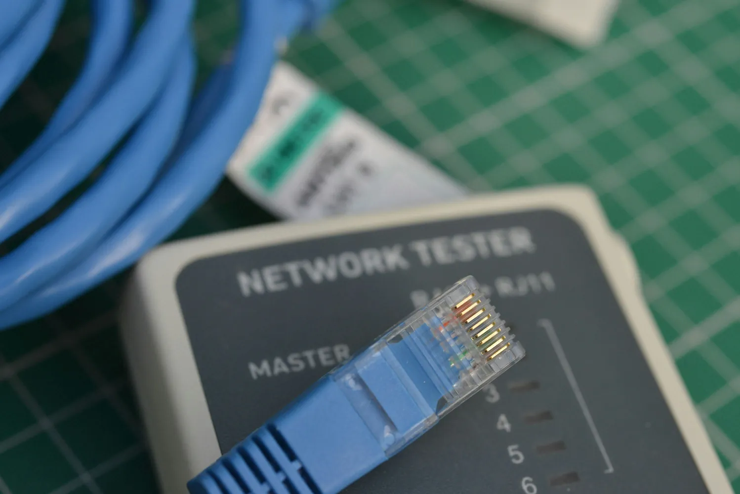 A network cable tester connected to a blue Ethernet lead on a green cutting mat