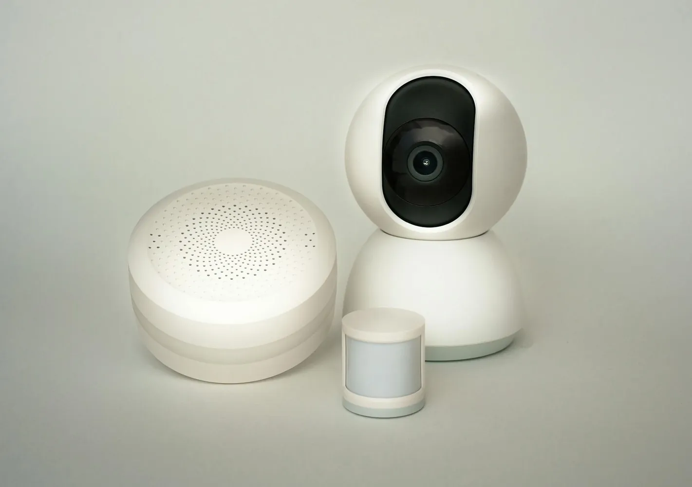 A white indoor security camera on a round base, standing on a shelf beside a small speaker