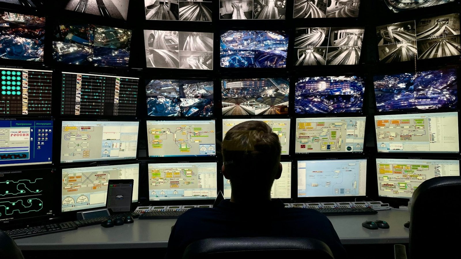 An analyst seated in front of a wall of monitors in a security operations centre, the room lit mainly by the screens