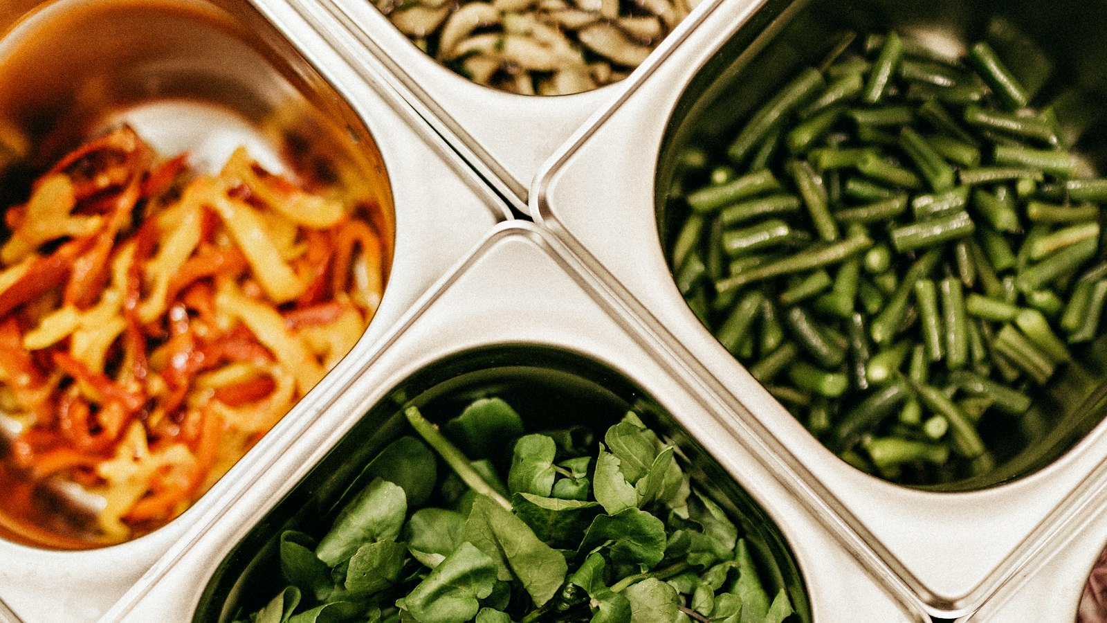 Stainless steel gastronorm containers holding peppers, green beans and salad leaves at a serving counter