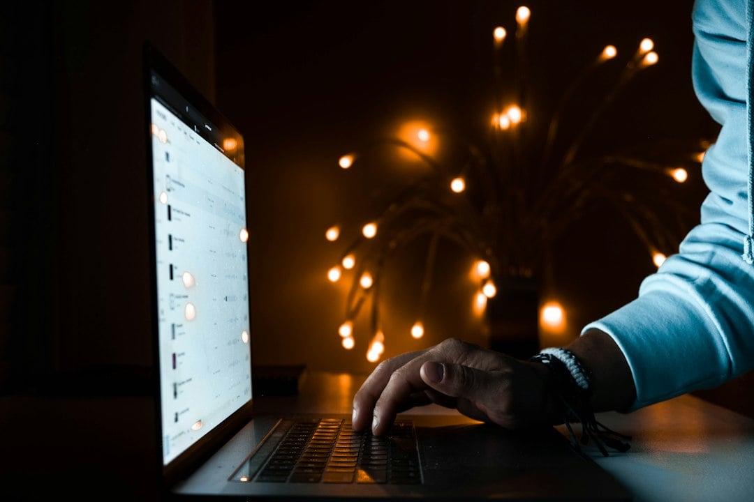 A person's hand typing on a glowing laptop keyboard in a darkened room
