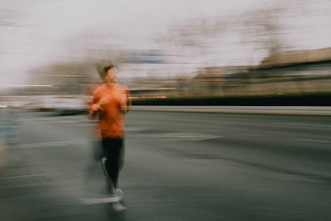 A runner in an orange long-sleeve top captured with motion blur while running along a road.