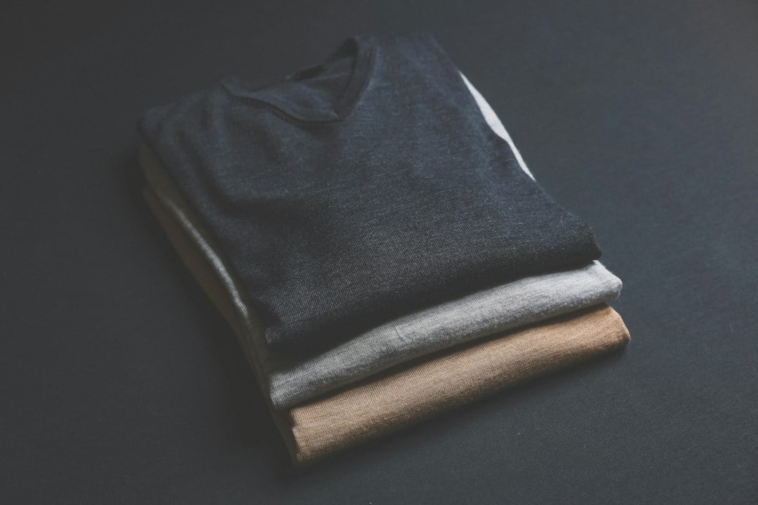 Three folded knit sweaters in navy, grey and camel stacked on a dark background.